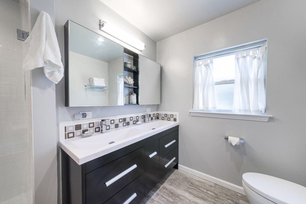 Mid-sized midcentury bathroom in Other with flat-panel cabinets, black cabinets, gray tile, porcelain tile, soapstone benchtops, white benchtops, a freestanding tub, a corner shower, a one-piece toilet, grey walls, vinyl floors, an integrated sink, multi-coloured floor and a hinged shower door.