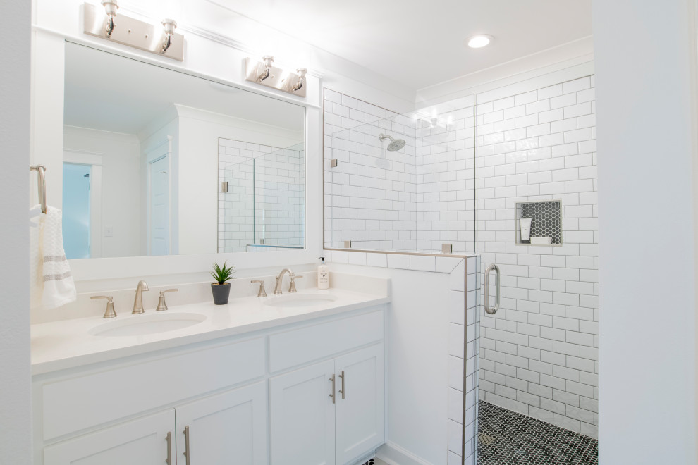 White tile and subway tile porcelain tile, black floor and double-sink bathroom photo with shaker cabinets, white cabinets, an undermount sink, granite countertops, a hinged shower door, white countertops and a built-in vanity