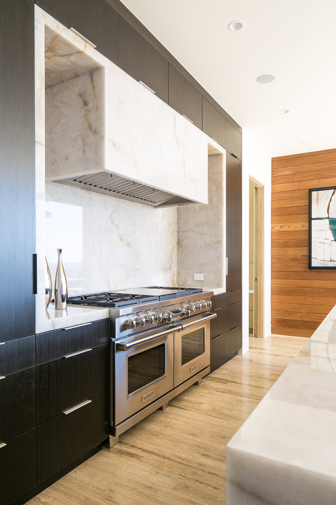 Contemporary galley kitchen in Orange County with flat-panel cabinets, black cabinets, white splashback, stainless steel appliances, with island and brown floor.