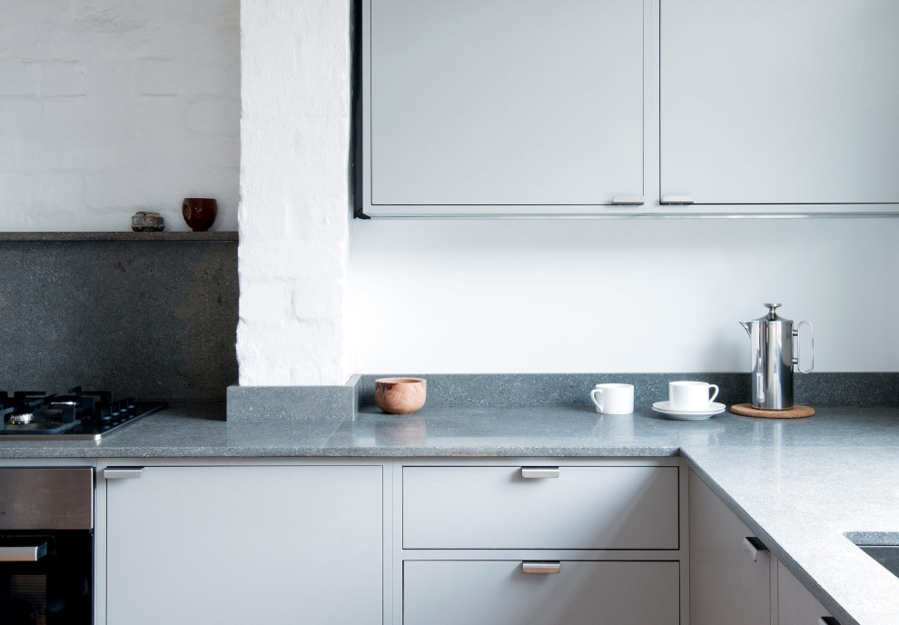 This is an example of a small contemporary l-shaped eat-in kitchen in London with a double-bowl sink, flat-panel cabinets, grey cabinets, limestone benchtops, grey splashback, limestone splashback, stainless steel appliances, cork floors, no island and grey benchtop.