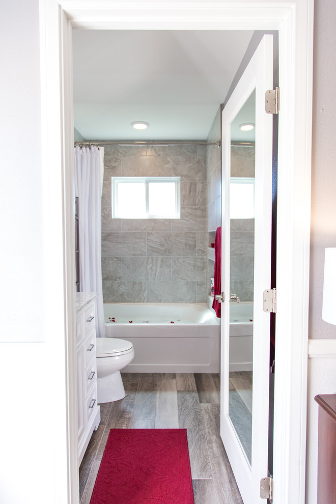 Photo of a small transitional master bathroom in Orange County with shaker cabinets, white cabinets, an alcove tub, a shower/bathtub combo, a two-piece toilet, gray tile, porcelain tile, grey walls, vinyl floors, an undermount sink, quartzite benchtops, brown floor and a shower curtain.