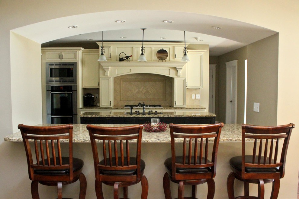 Open concept kitchen - mid-sized transitional galley open concept kitchen idea with an undermount sink, recessed-panel cabinets, white cabinets, granite countertops, beige backsplash, porcelain backsplash, stainless steel appliances, an island and beige countertops