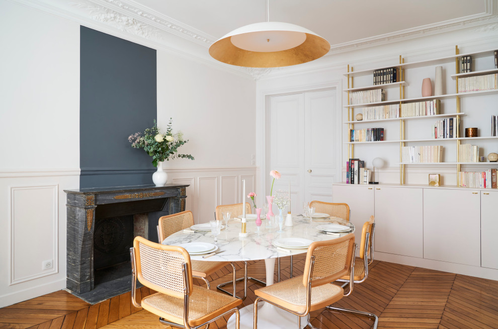 Exemple d'une salle à manger ouverte sur le salon chic avec un mur blanc, un sol en bois brun, une cheminée standard, un manteau de cheminée en pierre et un sol marron.