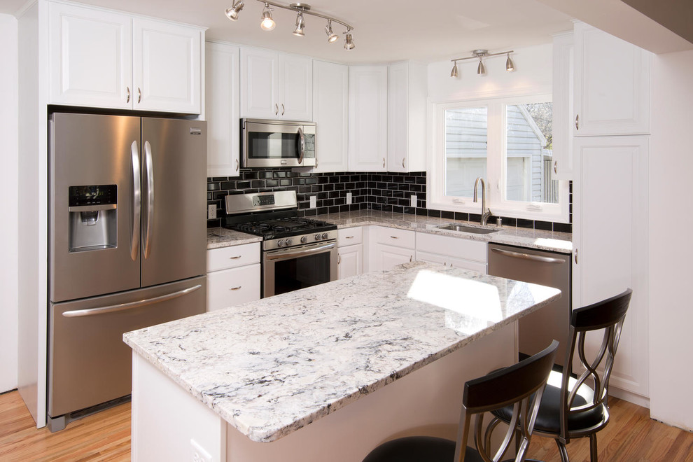 Inspiration for a small contemporary l-shaped eat-in kitchen in Minneapolis with an undermount sink, raised-panel cabinets, white cabinets, granite benchtops, black splashback, ceramic splashback, stainless steel appliances, light hardwood floors and with island.
