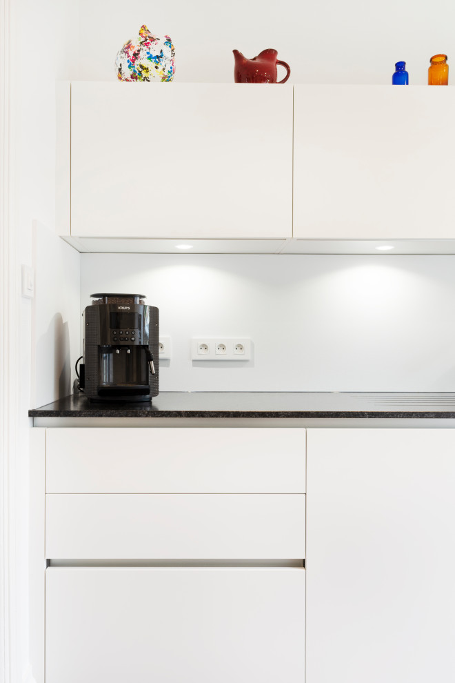 Design ideas for a medium sized modern galley kitchen in Nancy with white cabinets, granite worktops, white splashback and black worktops.