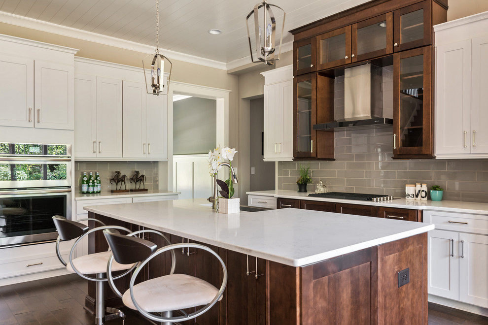 This is an example of a mid-sized arts and crafts l-shaped open plan kitchen in Charlotte with shaker cabinets, white cabinets, quartzite benchtops, grey splashback, glass tile splashback, stainless steel appliances, with island, a farmhouse sink, dark hardwood floors and brown floor.