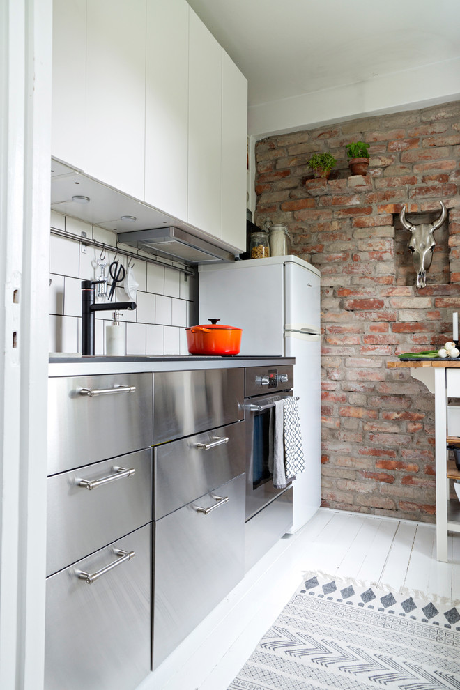 This is an example of a large scandinavian single-wall kitchen in Gothenburg with flat-panel cabinets, stainless steel cabinets, stainless steel benchtops, stainless steel appliances, painted wood floors and no island.