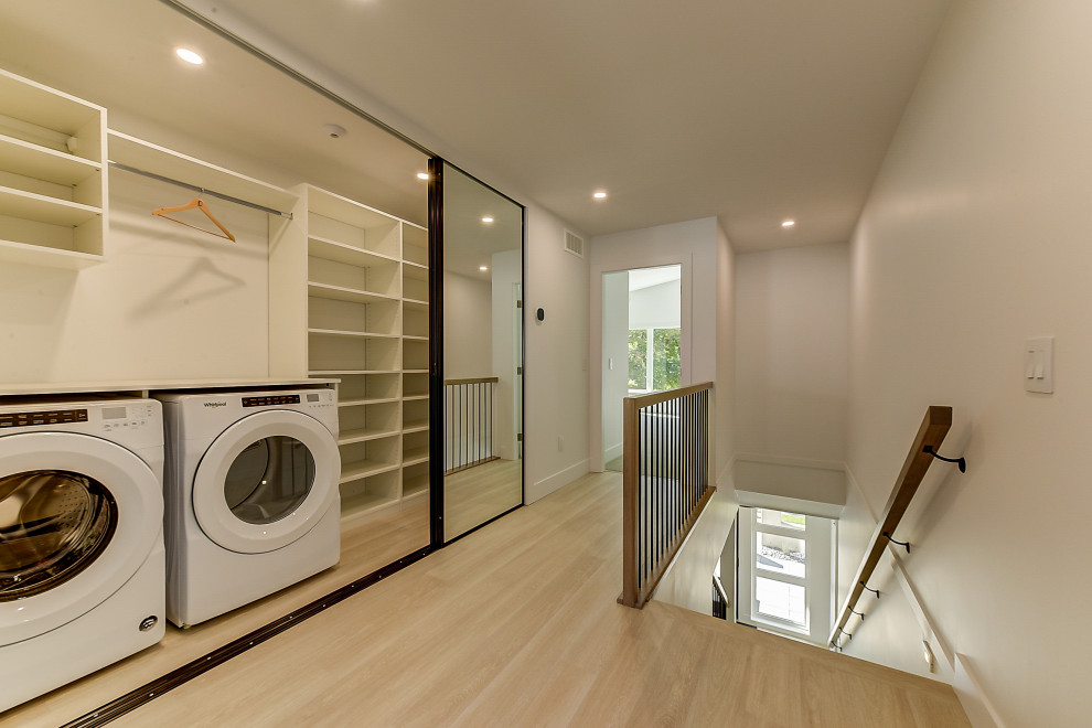 This is an example of a small modern single-wall laundry cupboard in Other with open cabinets, white cabinets, white walls, laminate floors, a side-by-side washer and dryer and brown floor.