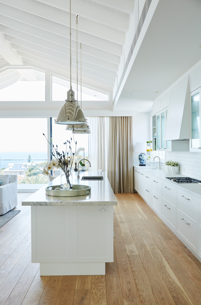 Design ideas for a large beach style single-wall open plan kitchen in Sydney with shaker cabinets, white cabinets, quartz benchtops, white splashback, ceramic splashback, with island and grey benchtop.