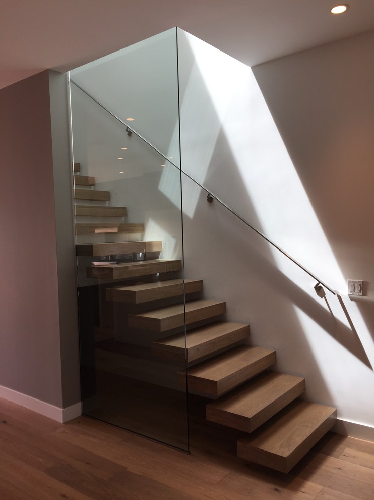 Large contemporary wood straight staircase in Los Angeles with open risers and glass railing.