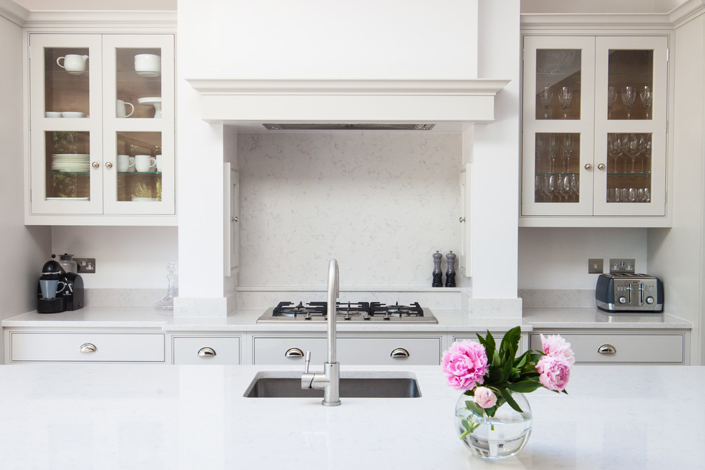 Inspiration for a large transitional single-wall kitchen in London with quartzite benchtops, with island, an undermount sink, glass-front cabinets, white cabinets, white splashback and stone slab splashback.