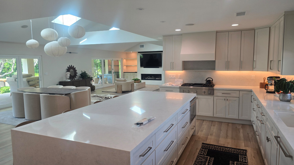 Mid-sized l-shaped vinyl floor and gray floor open concept kitchen photo in Orange County with an undermount sink, shaker cabinets, white cabinets, quartz countertops, white backsplash, quartz backsplash, white appliances, an island and white countertops