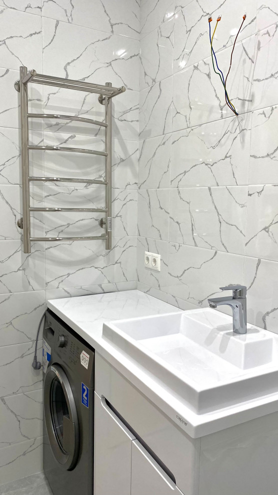 Пример оригинального дизайна: маленькая главная, серо-белая ванная комната со стиральной машиной в современном стиле с плоскими фасадами, белыми фасадами, угловой ванной, душем над ванной, белой плиткой, керамической плиткой, белыми стенами, полом из керамогранита, монолитной раковиной, столешницей из искусственного камня, серым полом, открытым душем, белой столешницей, тумбой под одну раковину и напольной тумбой для на участке и в саду