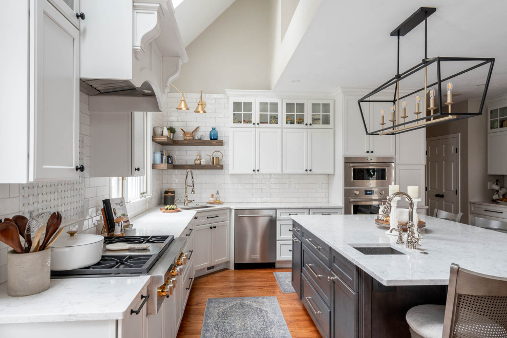 This is an example of an expansive traditional l-shaped open plan kitchen in Boston with a submerged sink, shaker cabinets, white cabinets, engineered stone countertops, white splashback, metro tiled splashback, stainless steel appliances, dark hardwood flooring, an island, brown floors, white worktops and a vaulted ceiling.