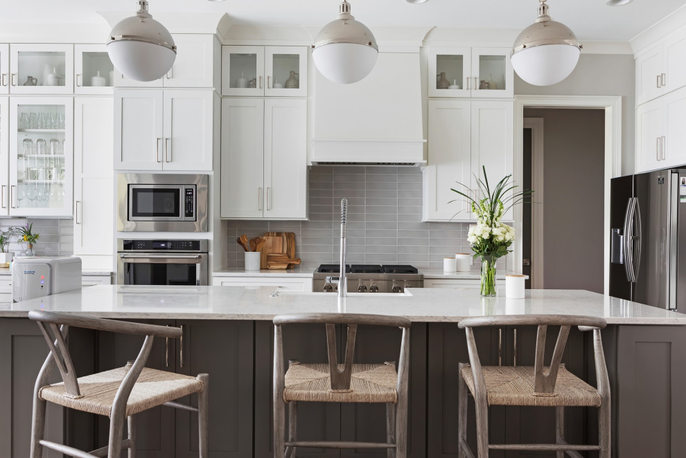 Inspiration for a mid-sized transitional single-wall light wood floor and brown floor kitchen remodel in Raleigh with glass-front cabinets, white cabinets, gray backsplash, glass tile backsplash, stainless steel appliances, an island and white countertops