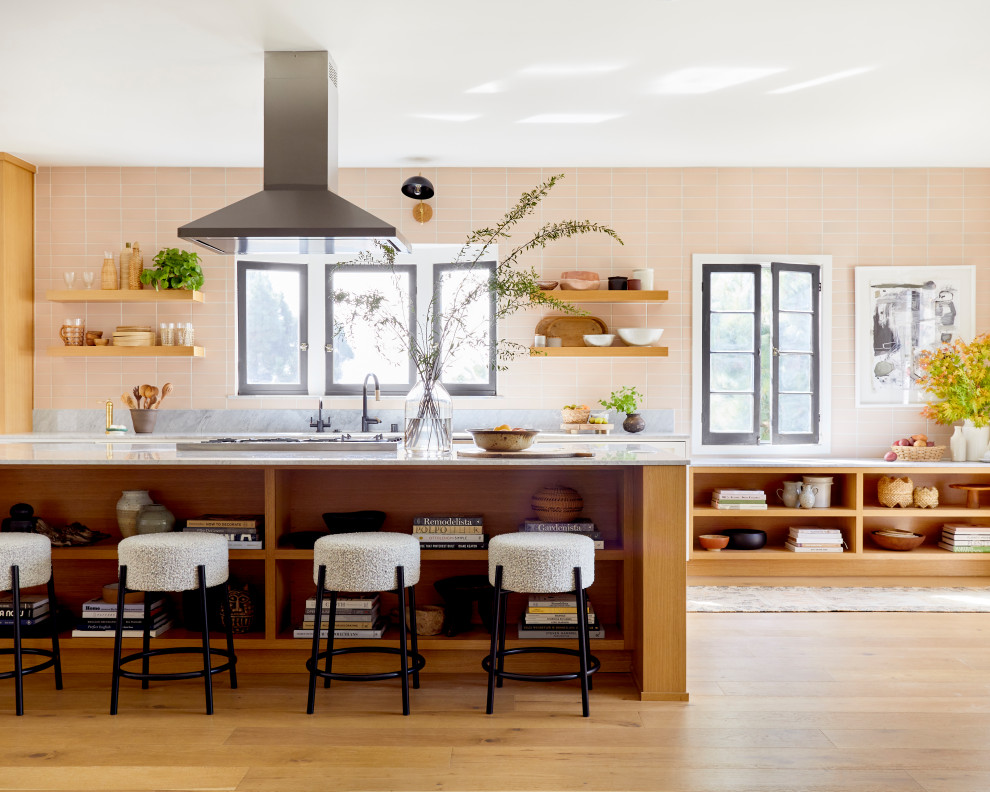Design ideas for a large eclectic single-wall open plan kitchen in Los Angeles with an undermount sink, light wood cabinets, beige splashback, ceramic splashback, stainless steel appliances, light hardwood floors, with island and white benchtop.