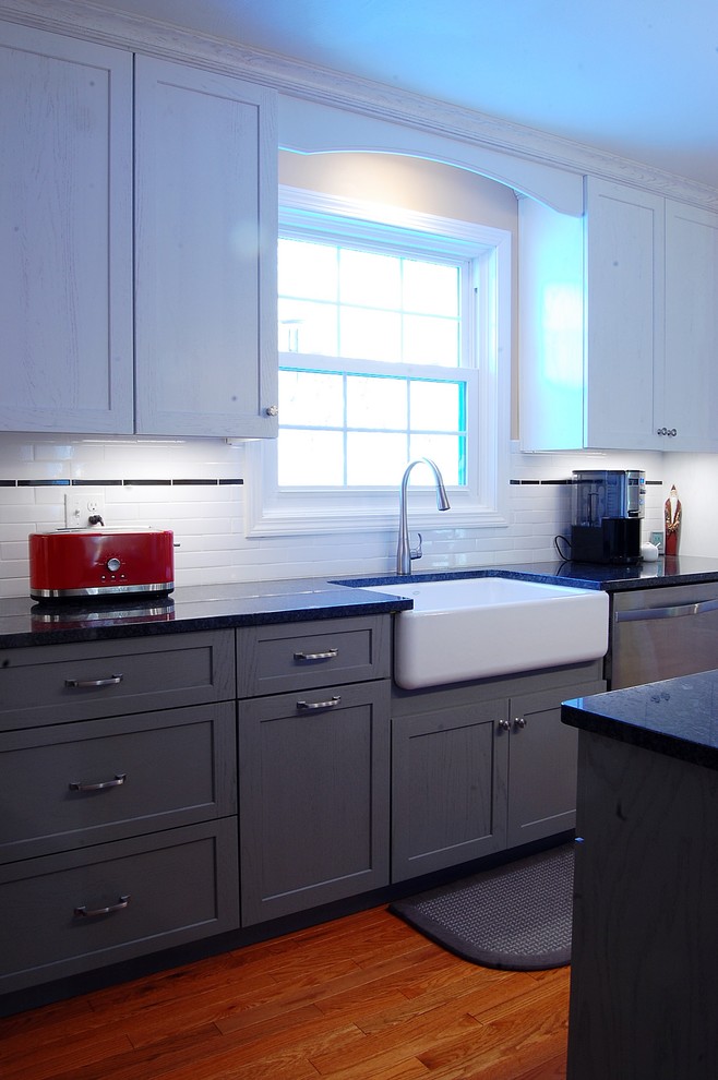 Example of a mid-sized transitional l-shaped medium tone wood floor eat-in kitchen design in Boston with a farmhouse sink, shaker cabinets, white cabinets, quartz countertops, white backsplash, subway tile backsplash, stainless steel appliances and an island