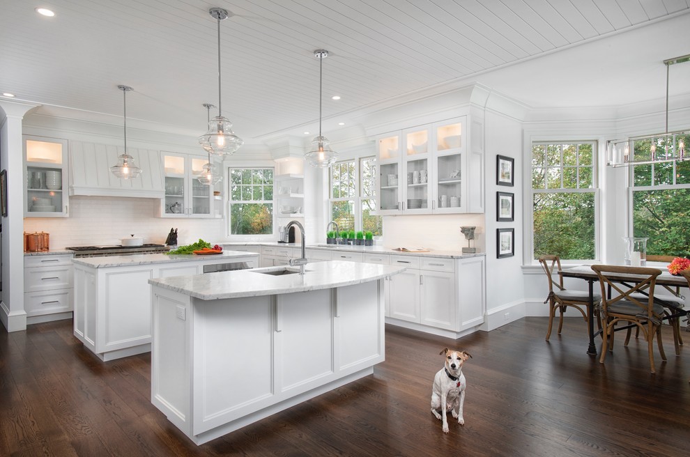 Photo of a mid-sized traditional u-shaped open plan kitchen in New York with an undermount sink, recessed-panel cabinets, white cabinets, marble benchtops, white splashback, subway tile splashback, dark hardwood floors, multiple islands, brown floor and white benchtop.