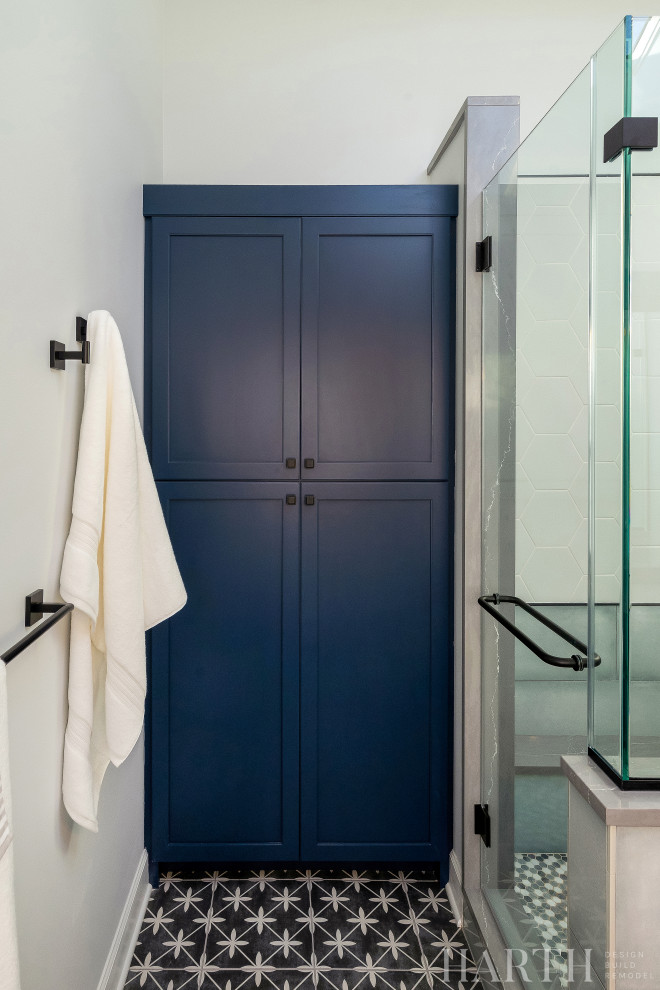 This is an example of a mid-sized transitional master bathroom in Philadelphia with shaker cabinets, blue cabinets, an alcove shower, a two-piece toilet, white tile, porcelain tile, grey walls, porcelain floors, an undermount sink, engineered quartz benchtops, grey floor, a hinged shower door, grey benchtops, a shower seat, a double vanity and a built-in vanity.
