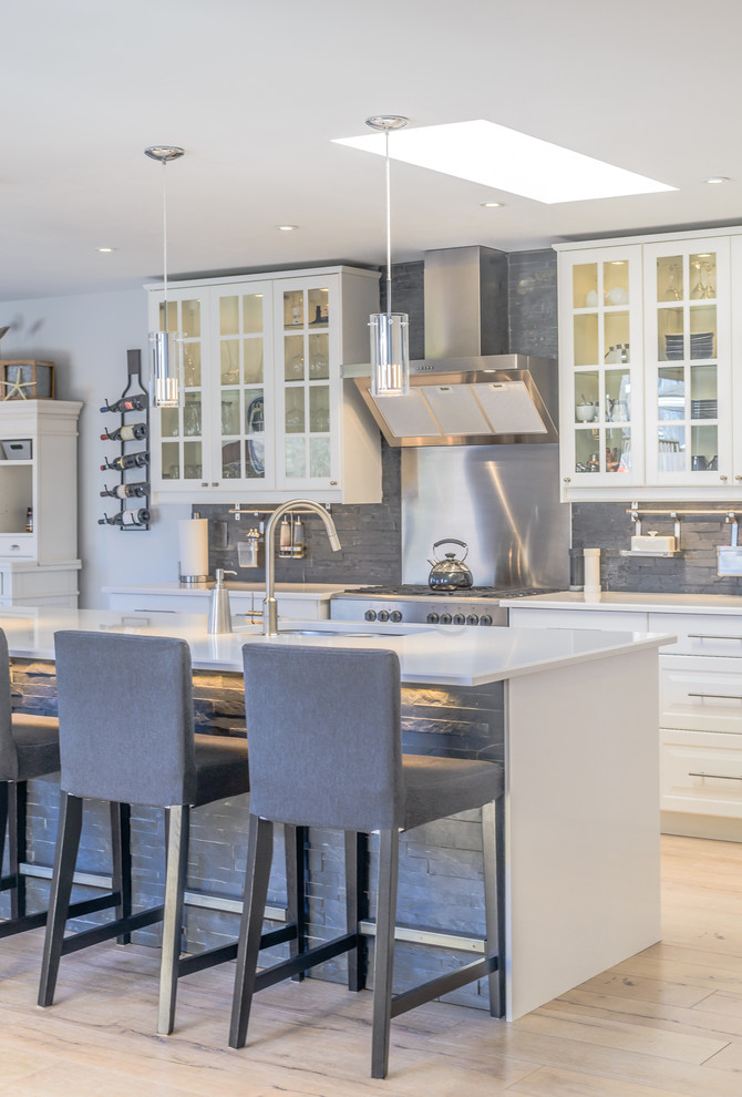 This is an example of an expansive beach style galley open plan kitchen in Toronto with a double-bowl sink, beaded inset cabinets, white cabinets, laminate benchtops, grey splashback, stone tile splashback, stainless steel appliances, light hardwood floors and with island.