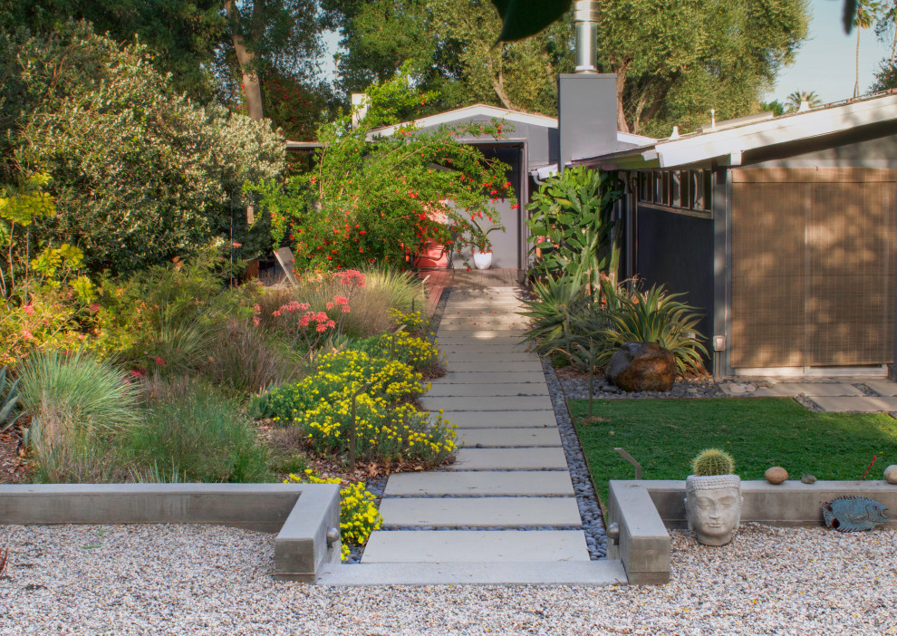 Photo of a large midcentury backyard full sun xeriscape for spring in Los Angeles with a retaining wall, concrete pavers and a metal fence.