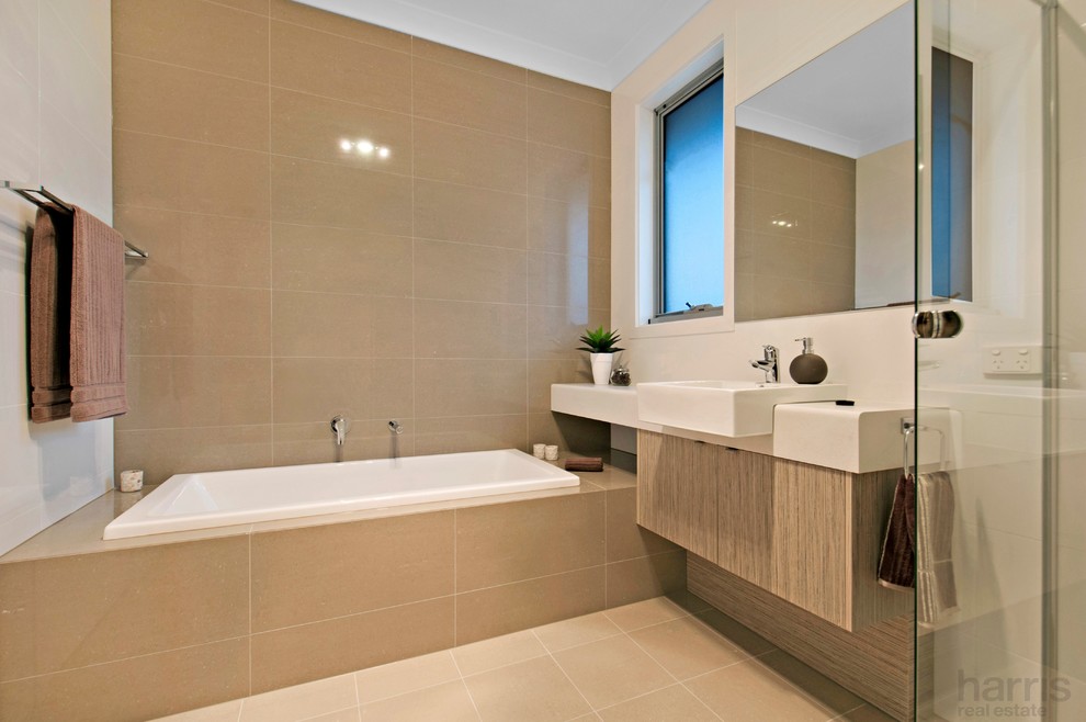 This is an example of a mid-sized contemporary master bathroom in Adelaide with a drop-in sink, flat-panel cabinets, light wood cabinets, a drop-in tub, a corner shower, beige tile, porcelain tile, white walls and porcelain floors.
