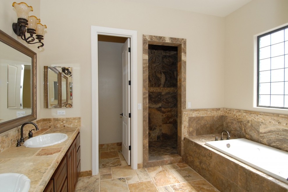 Photo of a large traditional master bathroom in Phoenix with beige tile, raised-panel cabinets, dark wood cabinets, a drop-in tub, an alcove shower, travertine, beige walls, travertine floors, a drop-in sink, tile benchtops, beige floor, a hinged shower door and beige benchtops.