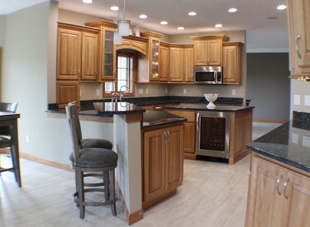 Photo of a mid-sized traditional u-shaped open plan kitchen in Chicago with an undermount sink, raised-panel cabinets, light wood cabinets, granite benchtops, stainless steel appliances, ceramic floors and with island.