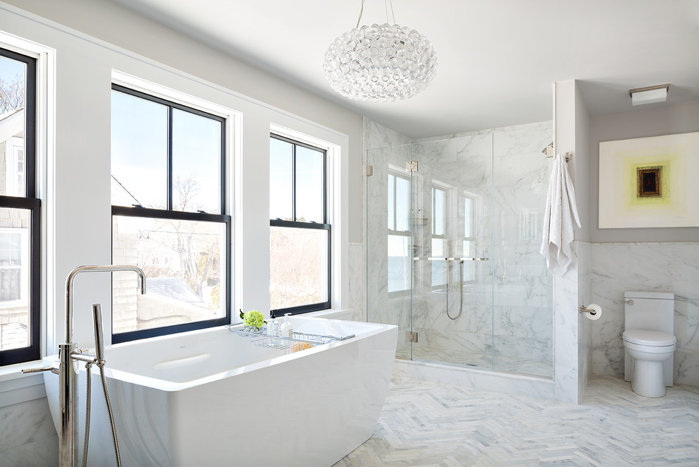 Photo of a large contemporary master bathroom in New York with white tile, stone tile, a freestanding tub, an alcove shower, a one-piece toilet and marble floors.