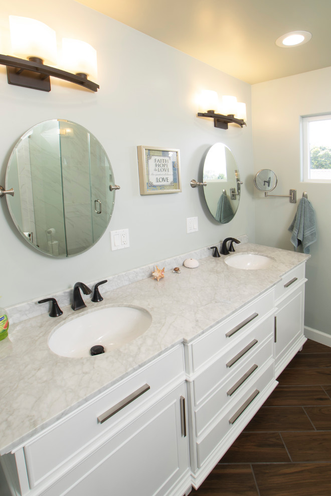 This is an example of a mid-sized contemporary master bathroom in Other with beaded inset cabinets, white cabinets, white tile, blue walls, ceramic floors, an undermount sink, marble benchtops, brown floor and white benchtops.