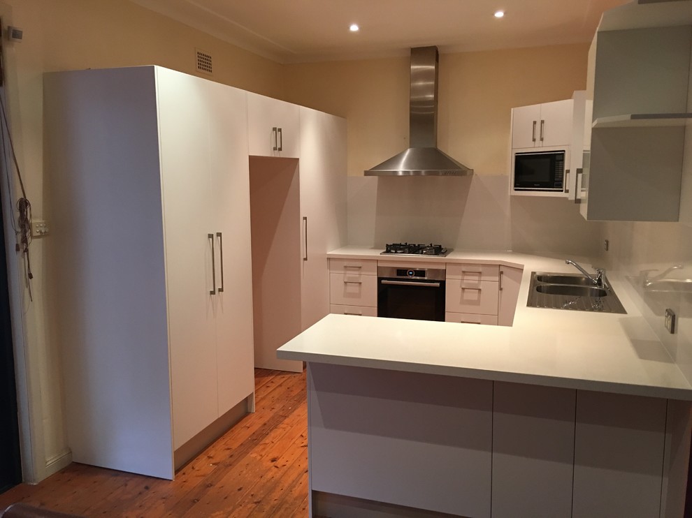 This is an example of a contemporary u-shaped kitchen in Sydney with a double-bowl sink, white splashback, stainless steel appliances, medium hardwood floors and a peninsula.
