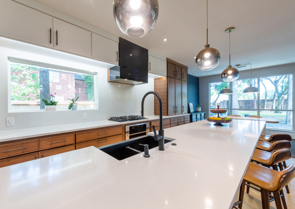 This is an example of a large midcentury eat-in kitchen in Dallas with a farmhouse sink, flat-panel cabinets, brown cabinets, quartz benchtops, white splashback, engineered quartz splashback, black appliances, light hardwood floors, with island, yellow floor and white benchtop.