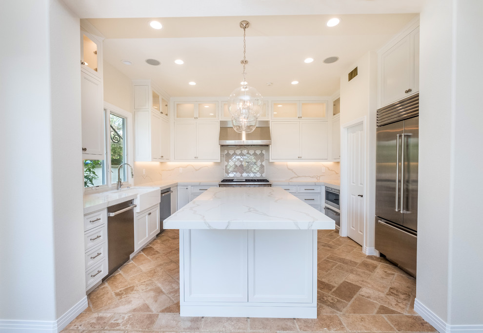 This is an example of a mid-sized transitional l-shaped separate kitchen in Orange County with recessed-panel cabinets, white cabinets, quartz benchtops, white splashback, marble splashback, stainless steel appliances, porcelain floors, with island, beige floor and a farmhouse sink.