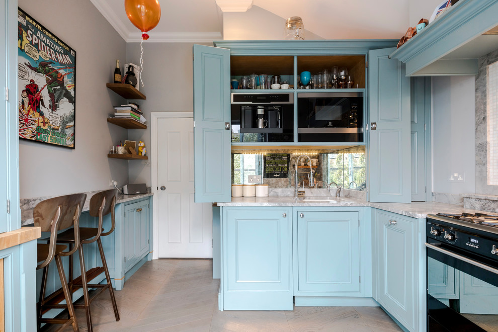 Photo of a small traditional eat-in kitchen in London with an undermount sink, raised-panel cabinets, blue cabinets, marble benchtops, grey splashback, marble splashback, black appliances, light hardwood floors, a peninsula, beige floor and grey benchtop.