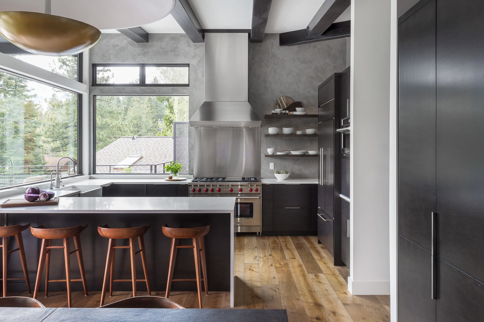Design ideas for a country u-shaped eat-in kitchen in Sacramento with a farmhouse sink, flat-panel cabinets, dark wood cabinets, concrete benchtops, window splashback, medium hardwood floors, a peninsula, grey benchtop and panelled appliances.