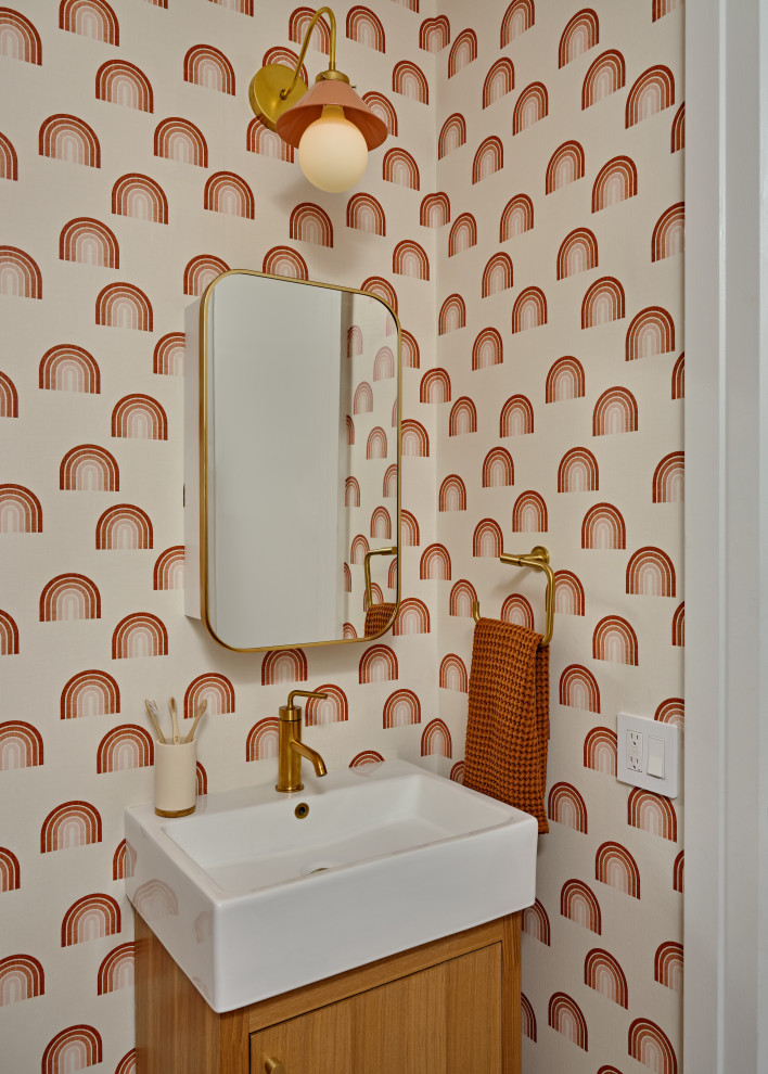 Trendy wallpaper powder room photo in New York with flat-panel cabinets, medium tone wood cabinets, multicolored walls and a console sink