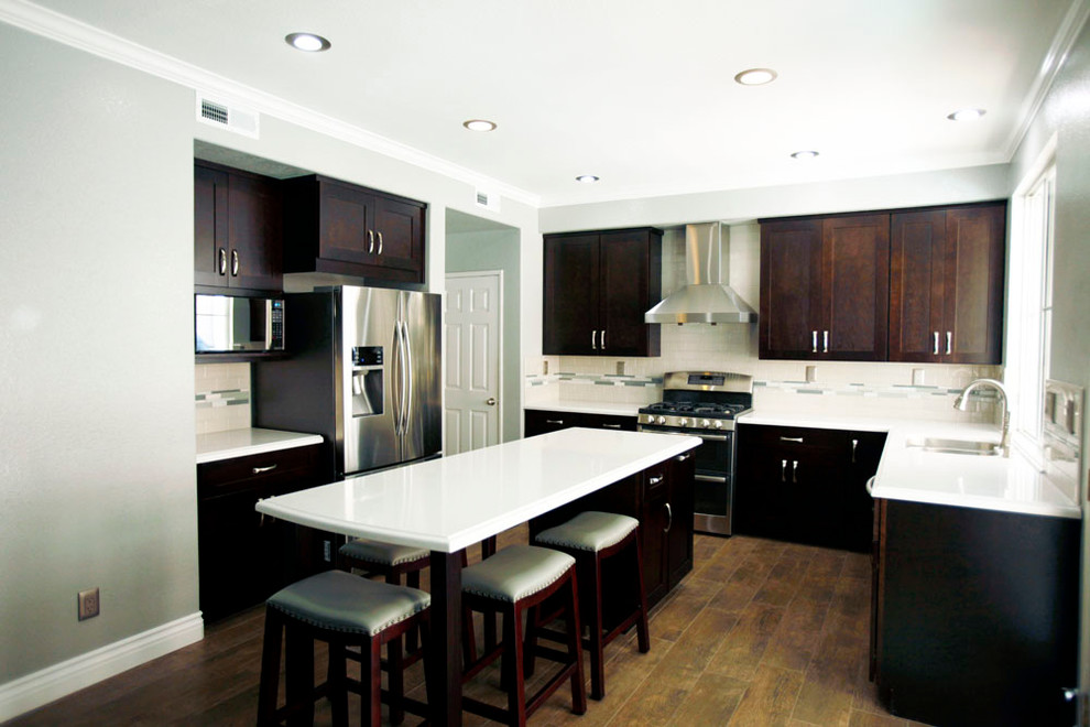Mid-sized transitional u-shaped medium tone wood floor eat-in kitchen photo in Los Angeles with dark wood cabinets, granite countertops, green backsplash, stainless steel appliances, an island, recessed-panel cabinets, ceramic backsplash and a double-bowl sink
