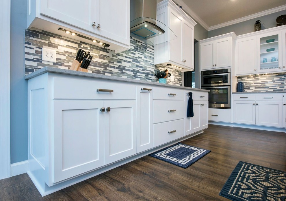 Inspiration for a mid-sized transitional single-wall dark wood floor and brown floor enclosed kitchen remodel in Columbus with a farmhouse sink, shaker cabinets, white cabinets, granite countertops, multicolored backsplash, matchstick tile backsplash, stainless steel appliances, an island and gray countertops
