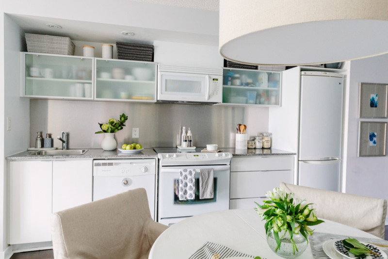 Inspiration for a small transitional galley eat-in kitchen in Toronto with a drop-in sink, flat-panel cabinets, white cabinets, granite benchtops, metallic splashback, metal splashback, white appliances, dark hardwood floors and no island.