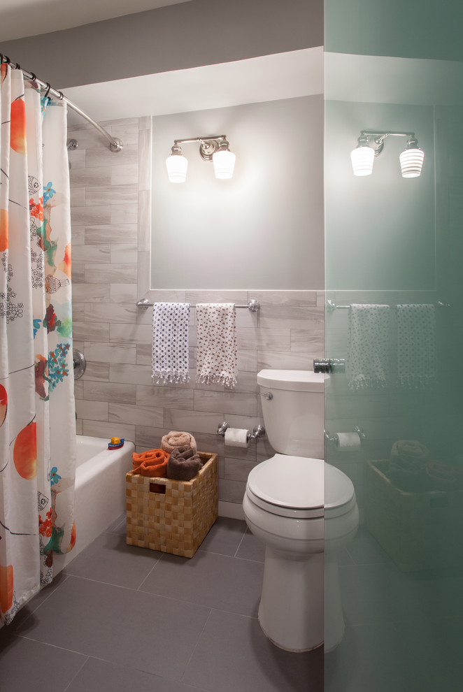 Tub/shower combo - small transitional kids' gray tile and porcelain tile ceramic tile and gray floor tub/shower combo idea with flat-panel cabinets, white cabinets, beige walls, marble countertops, a two-piece toilet and an undermount sink
