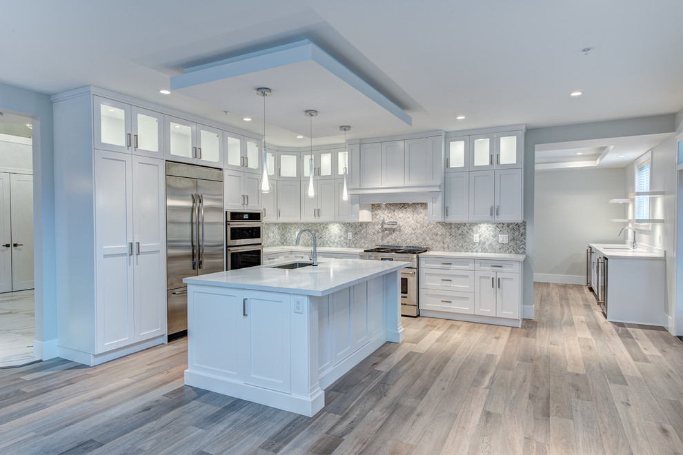 Inspiration for a large contemporary l-shaped eat-in kitchen in Vancouver with a drop-in sink, raised-panel cabinets, white cabinets, granite benchtops, grey splashback, ceramic splashback, stainless steel appliances, light hardwood floors and with island.