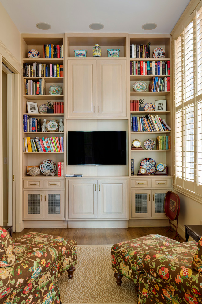 This is an example of a mid-sized traditional enclosed family room in Boston with a library, beige walls, medium hardwood floors and a built-in media wall.