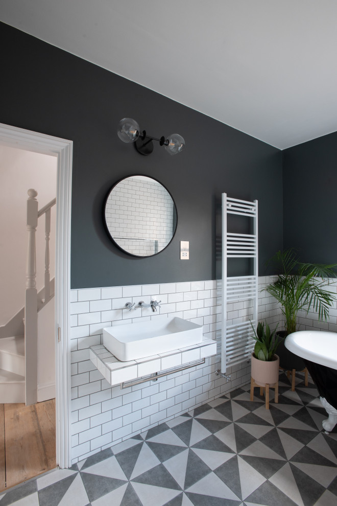This is an example of a large contemporary kids wet room bathroom in London with a freestanding tub, a wall-mount toilet, white tile, ceramic tile, black walls, ceramic floors, a vessel sink, tile benchtops, multi-coloured floor, an open shower, white benchtops and a single vanity.