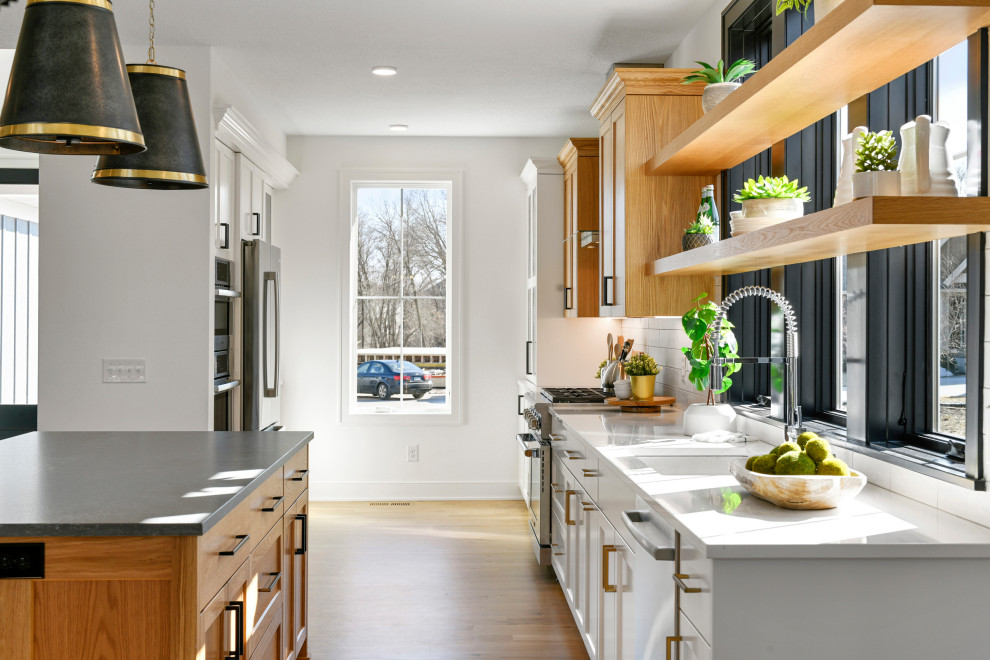 Design ideas for a mid-sized transitional galley eat-in kitchen in Minneapolis with a drop-in sink, recessed-panel cabinets, light wood cabinets, quartz benchtops, white splashback, ceramic splashback, stainless steel appliances, light hardwood floors, with island, brown floor and white benchtop.