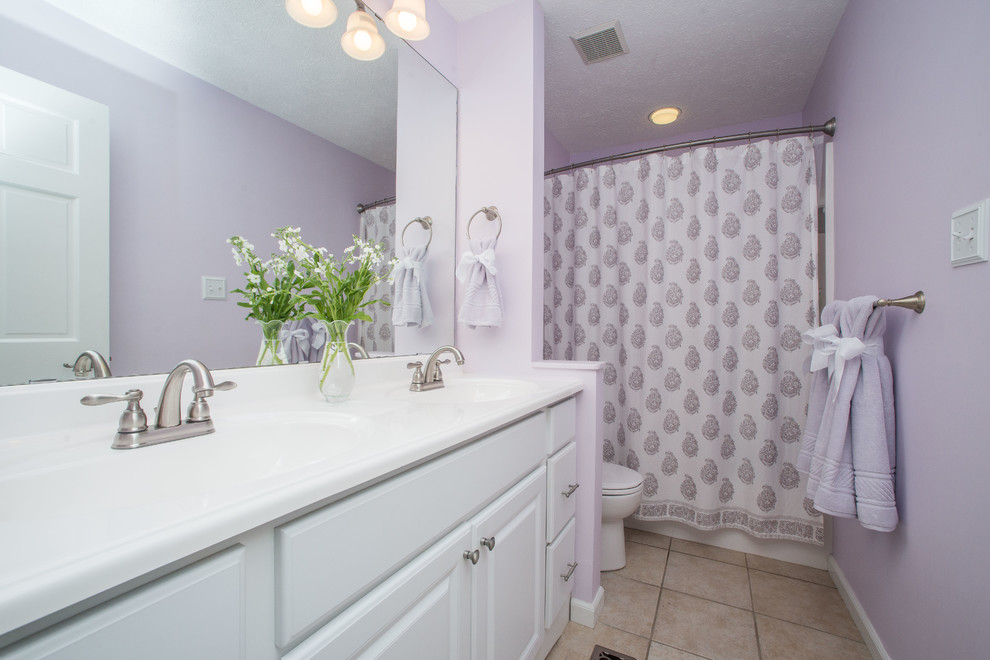 Photo of a mid-sized contemporary 3/4 bathroom in Other with raised-panel cabinets, white cabinets, an alcove tub, a shower/bathtub combo, a two-piece toilet, porcelain tile, purple walls, travertine floors, an undermount sink, solid surface benchtops, beige floor and a shower curtain.