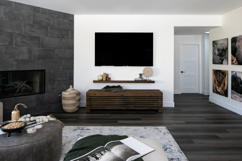 На фото: открытая гостиная комната среднего размера в современном стиле с белыми стенами, полом из винила, угловым камином, фасадом камина из плитки, телевизором на стене и коричневым полом