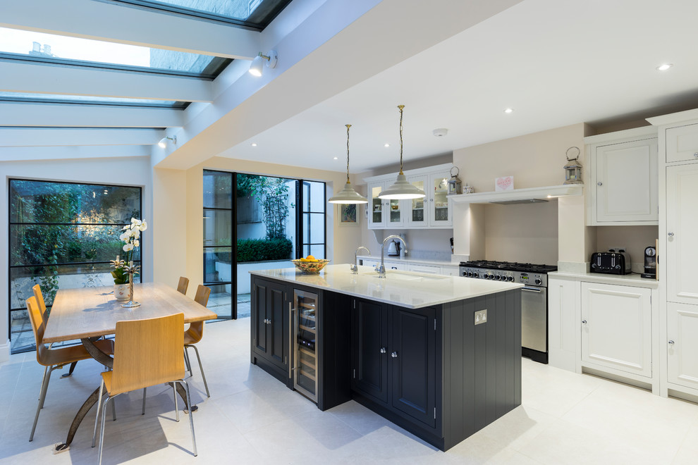 Photo of a large contemporary l-shaped eat-in kitchen in London with a farmhouse sink, shaker cabinets, white cabinets, quartzite benchtops, stainless steel appliances, with island and beige floor.