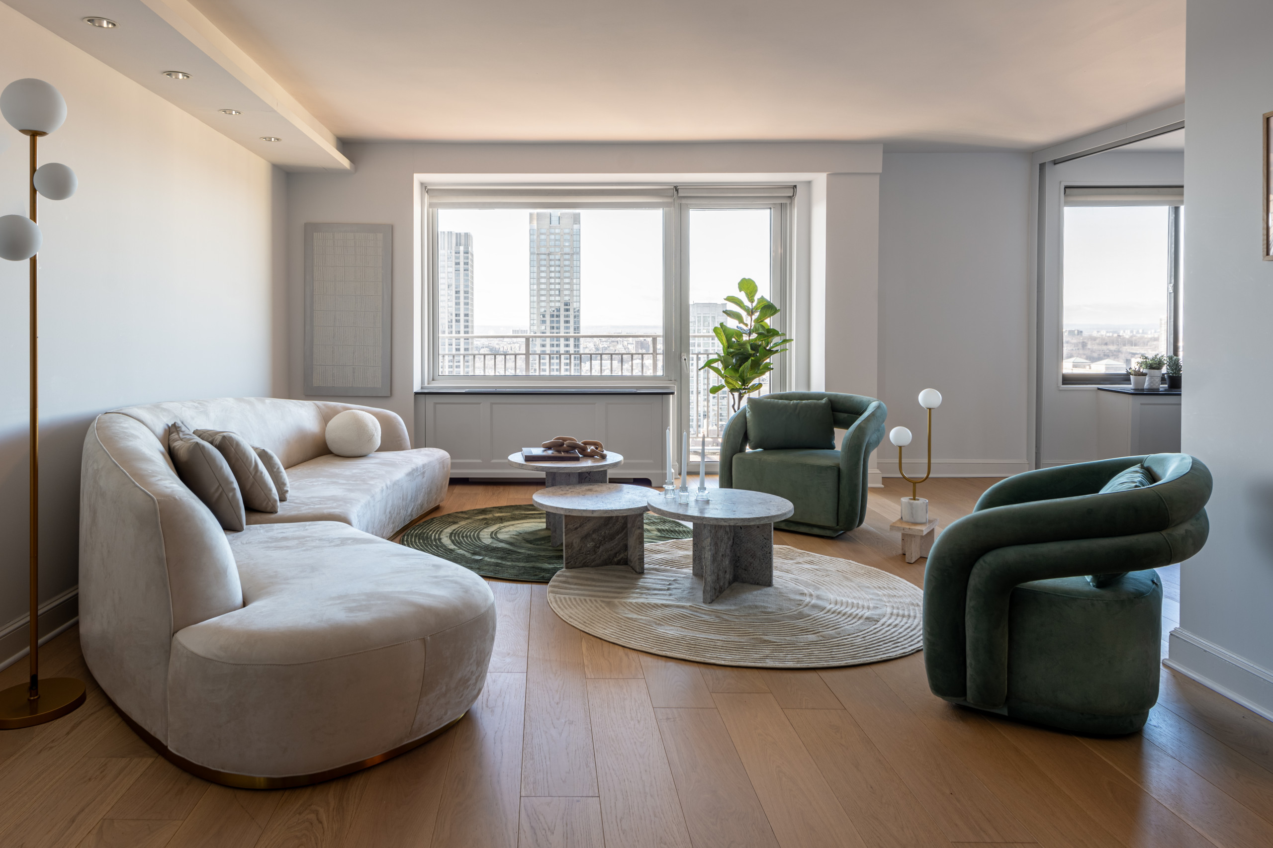 This living space is a perfect blend of modern sophistication and inviting comfort. A curvaceous cream sofa anchors the room, complemented by bold green velvet armchairs for a touch of color. Layered
