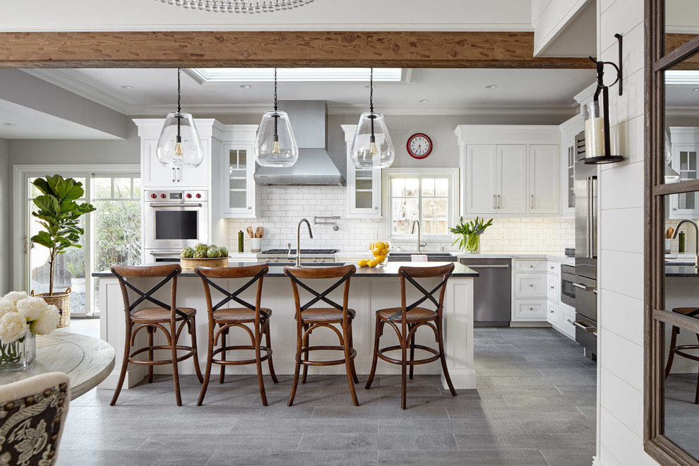 Beach style l-shaped open plan kitchen in San Francisco with a farmhouse sink, recessed-panel cabinets, white cabinets, white splashback, subway tile splashback, with island, grey floor and white benchtop.
