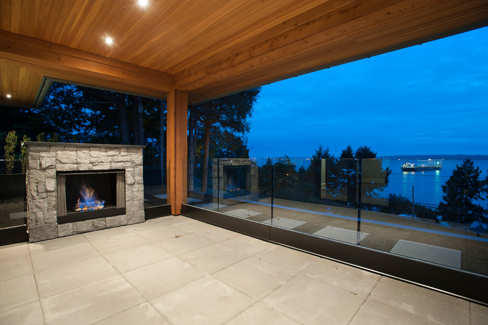 This is an example of an expansive transitional backyard deck in Vancouver with a fire feature and a roof extension.